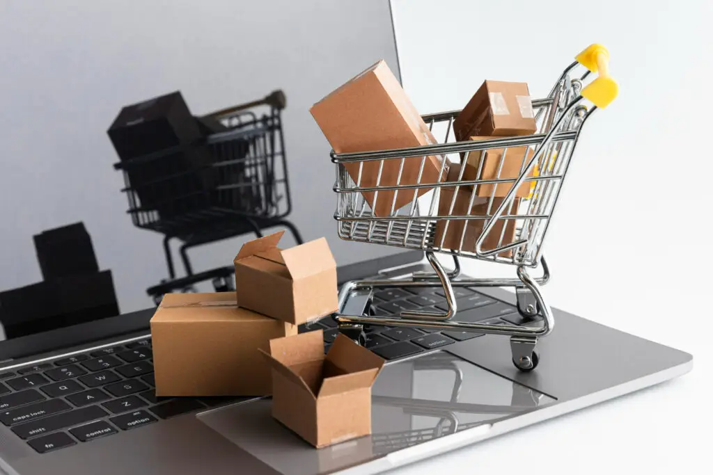 Miniatur keranjang belanja berisi kotak paket di atas keyboard laptop sebagai simbol e-commerce dan dropshipping