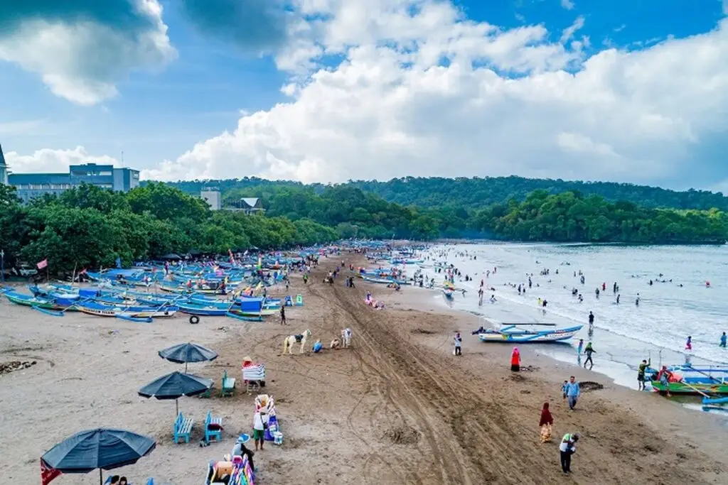 Pantai Pangandaran yang ramai pengunjung dengan banyak perahu dan aktivitas di tepi pantai.