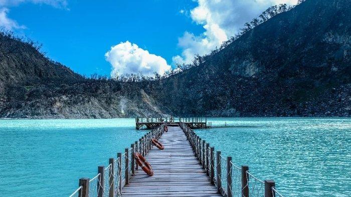 Jembatan kayu di atas danau berwarna biru di kawasan wisata Ciwidey, dikelilingi pegunungan dan langit cerah.