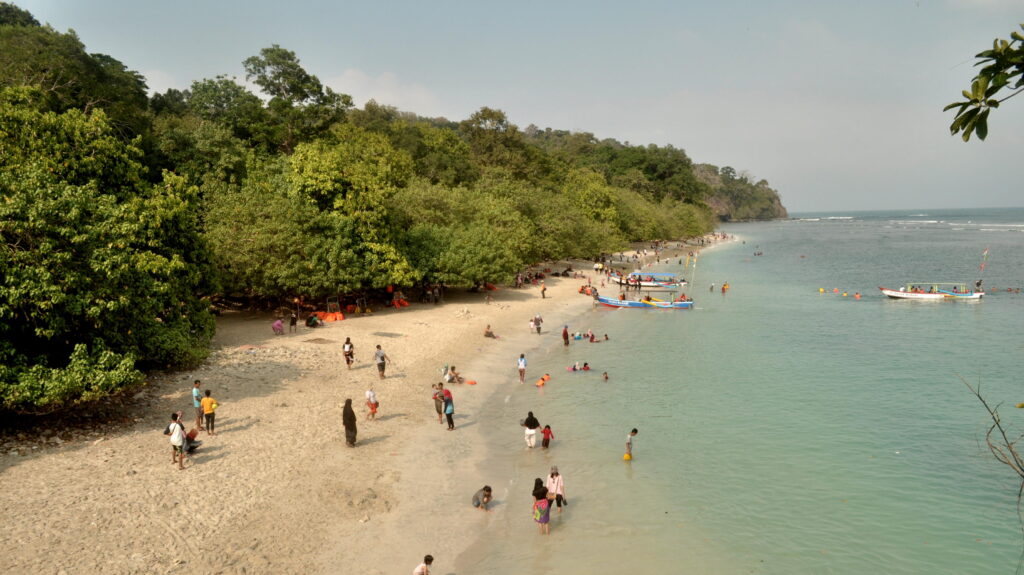Pantai Pangandaran dengan hamparan pasir dan pengunjung yang menikmati suasana pantai.